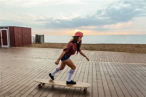 Trendy Girl Riding A Longboard By The Beach At Sunrise Del