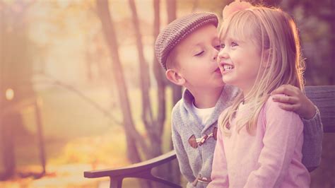 Cute Little Boy Is Kissing A Smiley Girl Sitting On Wooden Bench Wearing Ash And Pink Dress Hd