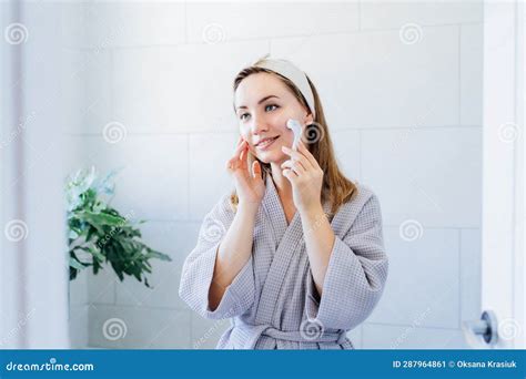 Young Woman In Bathrobe Looking In Mirror And Making Face Massage With Micro Needle Meso Derma