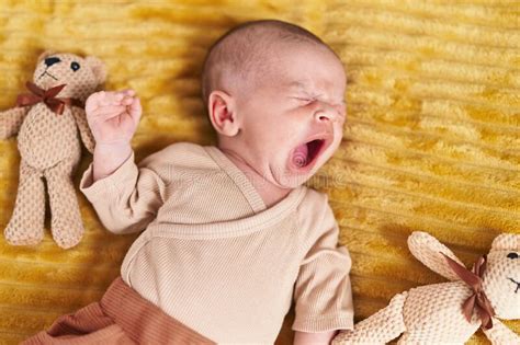 Adorable Caucasian Baby Lying On Bed Yawning At Bedroom Stock Photo