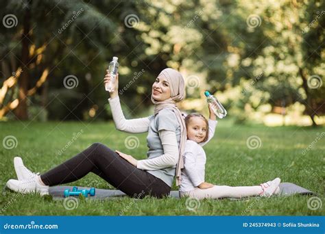 Arab Mom And Her Daughter Sitting On Gray Carrymat In The Summer Park