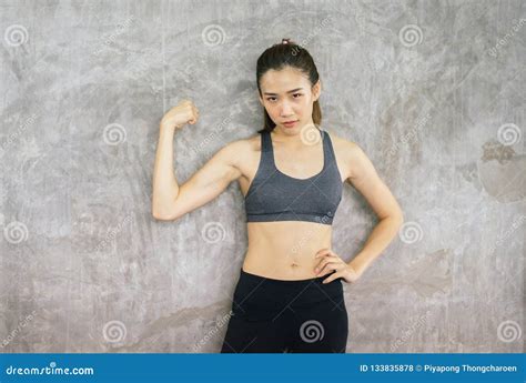 Strong Asian Woman Posture Standing And Lifting Up Her Arms And Exercises Muscle At Gym Stock