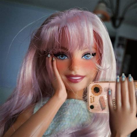 a barbie doll with pink hair and blue eyes holding a cell phone in front of her face