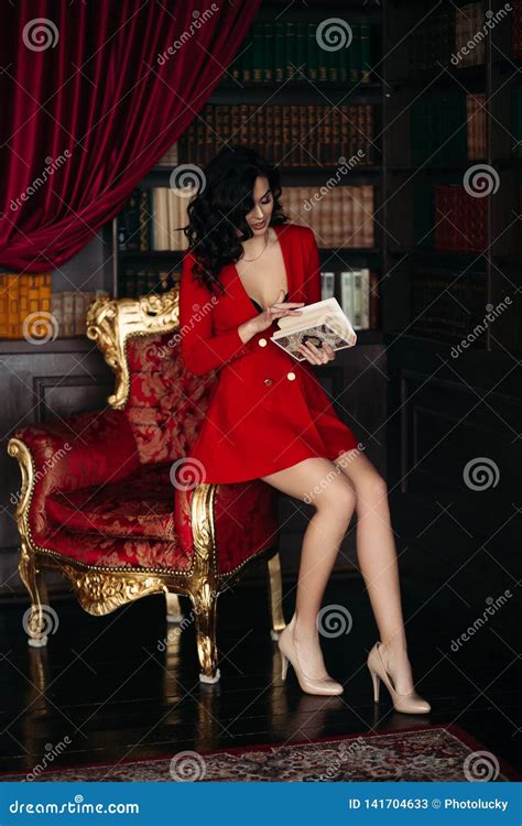 Elegant Brunette In Red Sitting On And Holding A Book Stock Image