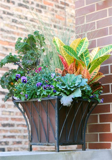 An Iron Planter With Plants In It Sitting On The Side Of A Brick Building
