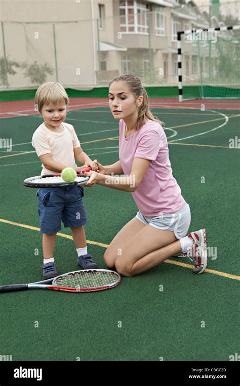 A Mother Teaching Her Son How To Balance A Tennis Ball On A Racket