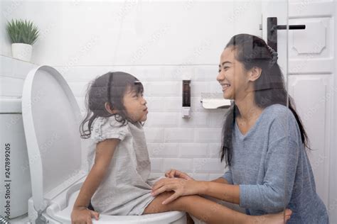 Asian Woman Help Her Daughter To Sit On The Toilet While Peeing Stock