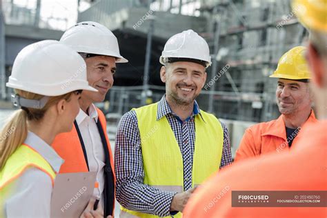 smiling engineers and construction workers meeting at construction site — woman industrial