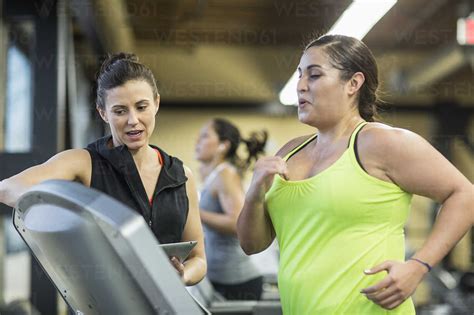 Trainer Instructing Woman Exercising On Treadmill In Gym Stock Photo