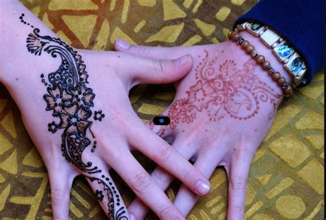two hands with henna tattoos on them one is holding the other s hand