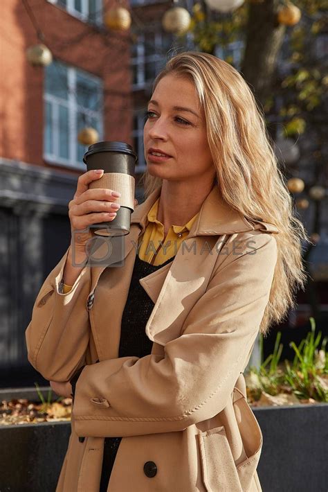 Caucasian Attractive Woman In Beige Trench Coat Holding Cup Of Coffee Outdoors Ad Holding
