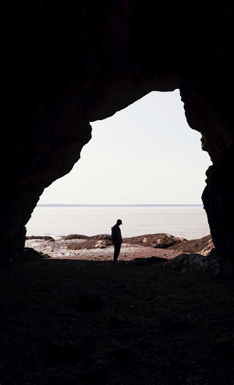 Silhouette Of Person Standing On Cave Entrance Across Horizon Photo
