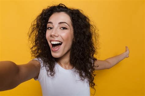 premium photo pretty woman 20s with curly hair laughing and taking selfie photo isolated on yellow