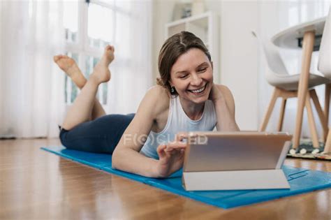 Delighted Slim Female Lying On Mat And Browsing Tablet While Choosing