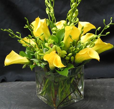 A Glass Vase Filled With Yellow Flowers On Top Of A Table Next To A