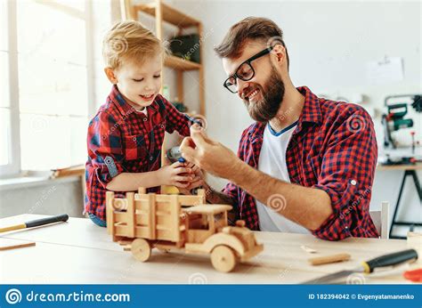 Cheerful Man With Kid Making Wooden Toys In Workshop Stock Photo
