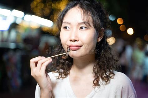 Portrait Of Asian Solo Hipster Traveller Holding A Fried Roasted Insect Stick On Street In