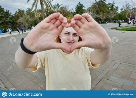 Young White Woman Makes A Heart Shape With Her Fingers For A Photo