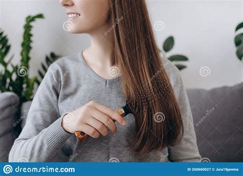 Beautiful Young Woman Brushing Hair With Wooden Brush Sitting On Cozy Sofa At Home Smiling