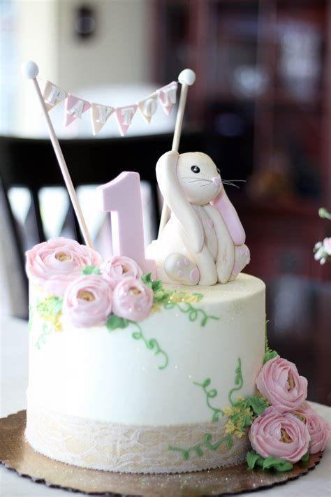 A White Cake Decorated With Pink Flowers And A Bunny On Top Is Sitting