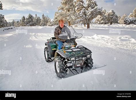 A Senior Citizen Plows Snow With An Atv All Terrain Vehicle After A