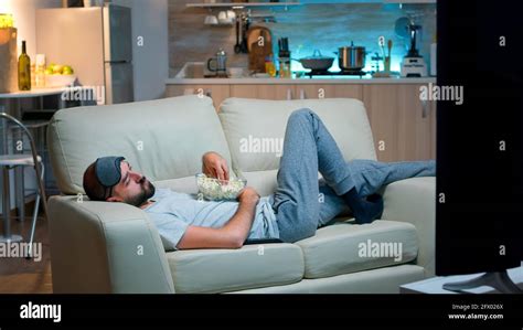 Man Lying On Sofa Falling Asleep In Fron Of The Tv With Popcorn Bowl