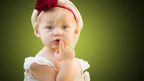 Cute Little Girl Baby Is Keeping Finger On Lips In Green Blur
