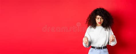 Worried Young Woman With Curly Hairstyle Looking Down And Pointing At