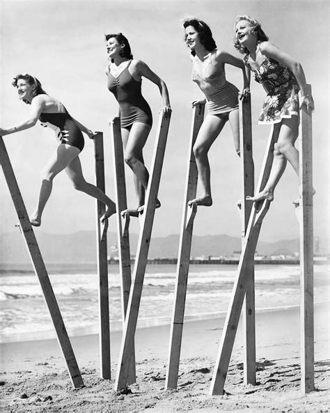 Four Women In Bathing Suits Standing On Stilts At The Beach All