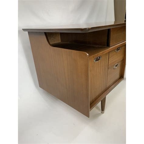 Like the a floating top which has an unusual shape, a brass support arm and special legs on the left side, three drawers (one small sized and two bigger sized) with sculpted 'smiling' handles and on the outer right side small book shelves. 1950s Mid Century Modern Hooker Furniture 
