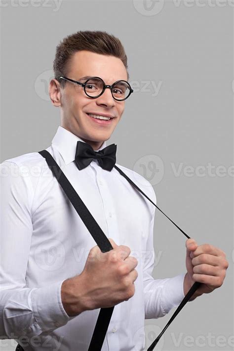 Confident Nerd Cheerful Young Man In Bow Tie Adjusting His Suspenders And Smiling At Camera