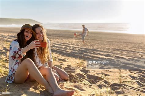 Two Best Friends Sitting On The Beach Taking Selfie With Smartphone