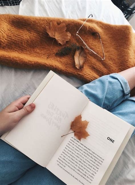 A Person Sitting On A Bed Reading A Book With An Autumn Leaf Attached To It