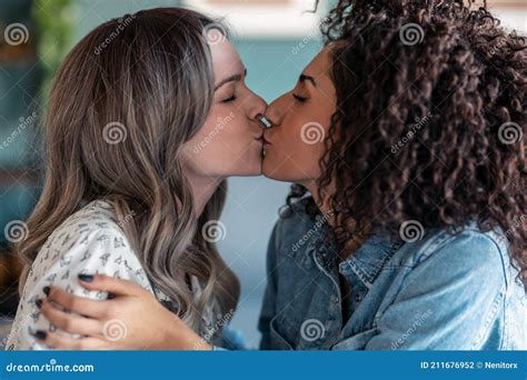 Two Beautiful Happy Woman Kissing Each Other While Loving Sitting In Living Room At Home Stock