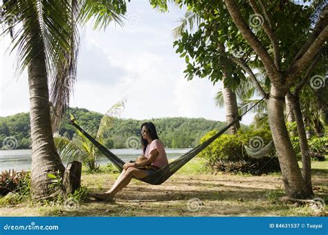 Asian Women Sit And Relaxing On Furniture Hammock Hanging Between Palm