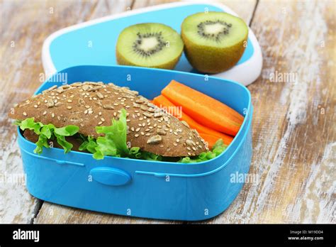 Healthy Packed Lunch Box Containing Brown Cheese Sandwich Crunchy Carrots And Kiwi Fruit Stock