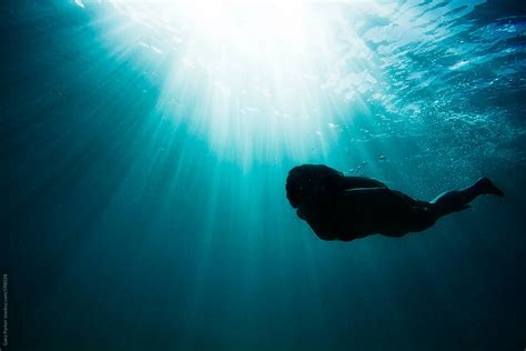 Girl Swimming Under Water In The Ocean As The Sun Rays Shine Down