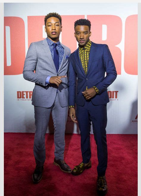 Two Men Standing Next To Each Other On A Red Carpet