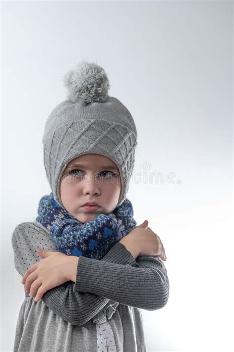 Upset Little Girl In A Gray Hat Wrapped In A Scarf On A White