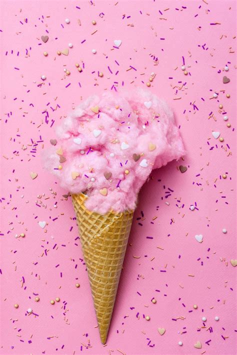 an ice cream cone filled with pink and gold sprinkles on a pink background