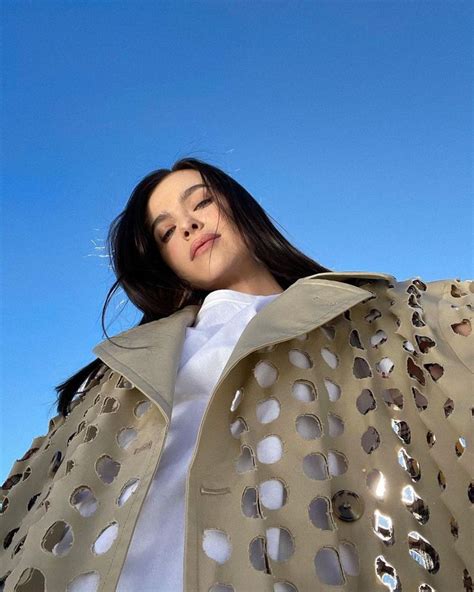 A Woman With Her Eyes Closed Standing In Front Of A Blue Sky Wearing A Beige Jacket