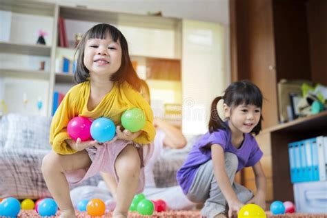 an asian girl enjoys playing and having fun in her home living room with colorful balls stock