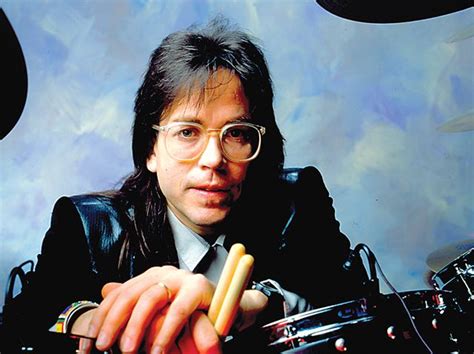 A Man With Long Hair And Glasses Is Holding A Drum Set In Front Of Him