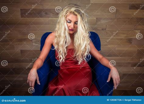 Young Blonde Woman Sits On Armchair Pensive Girl In Elegant Red Dress