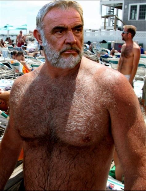 An Older Man With White Hair And Beard Standing In Front Of A Beach Full Of People