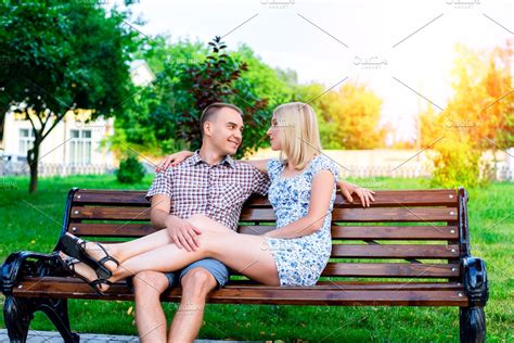 Young Couple Man And Woman Sitting On A Bench Hugging In Park Ribbon Declaration Of Love