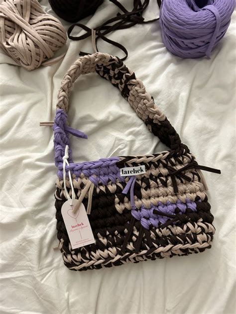 A Crocheted Purse Sitting On Top Of A Bed Next To Balls Of Yarn
