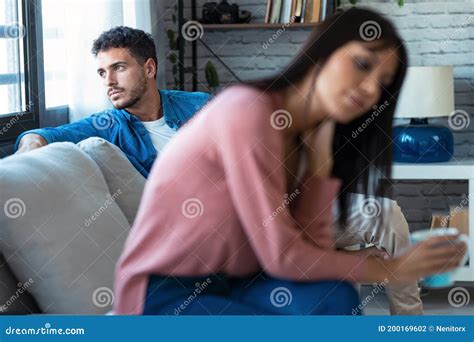 Angry Young Couple Sitting On Couch Together And Looking To Opposite