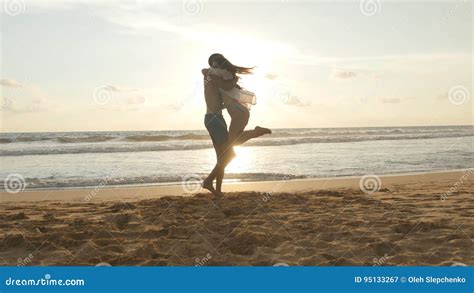 Young Couple Is Running On The Beach Man Hug And Spin Around His Woman On Sunset Girl Jumps