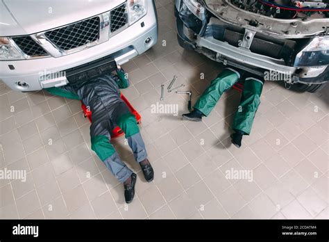 Mechanics In Uniform Lying Down And Working Under Car At The Garage
